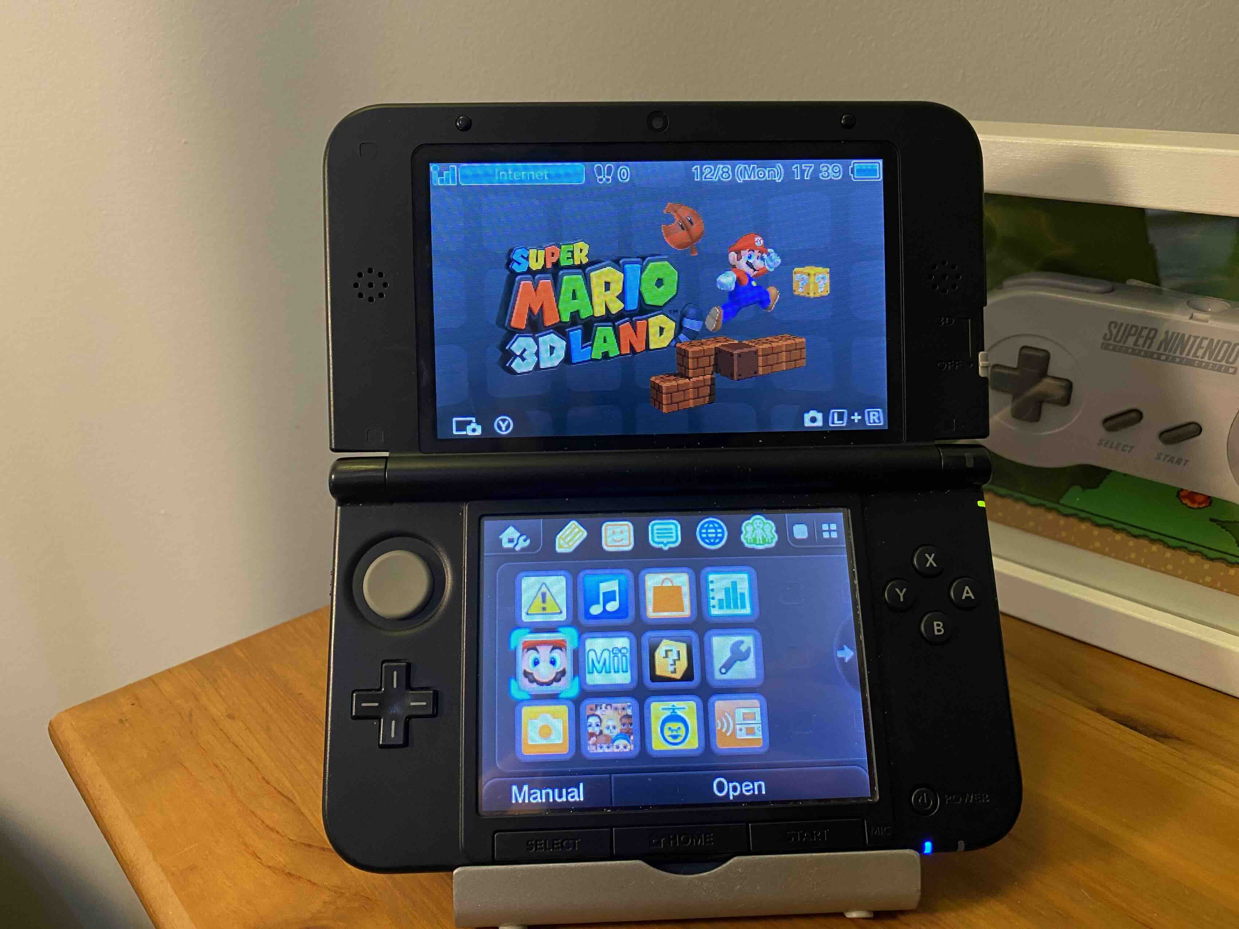 A black Nintendo 3DS on a stand showing the selection screen for Super Mario 3D Land.
