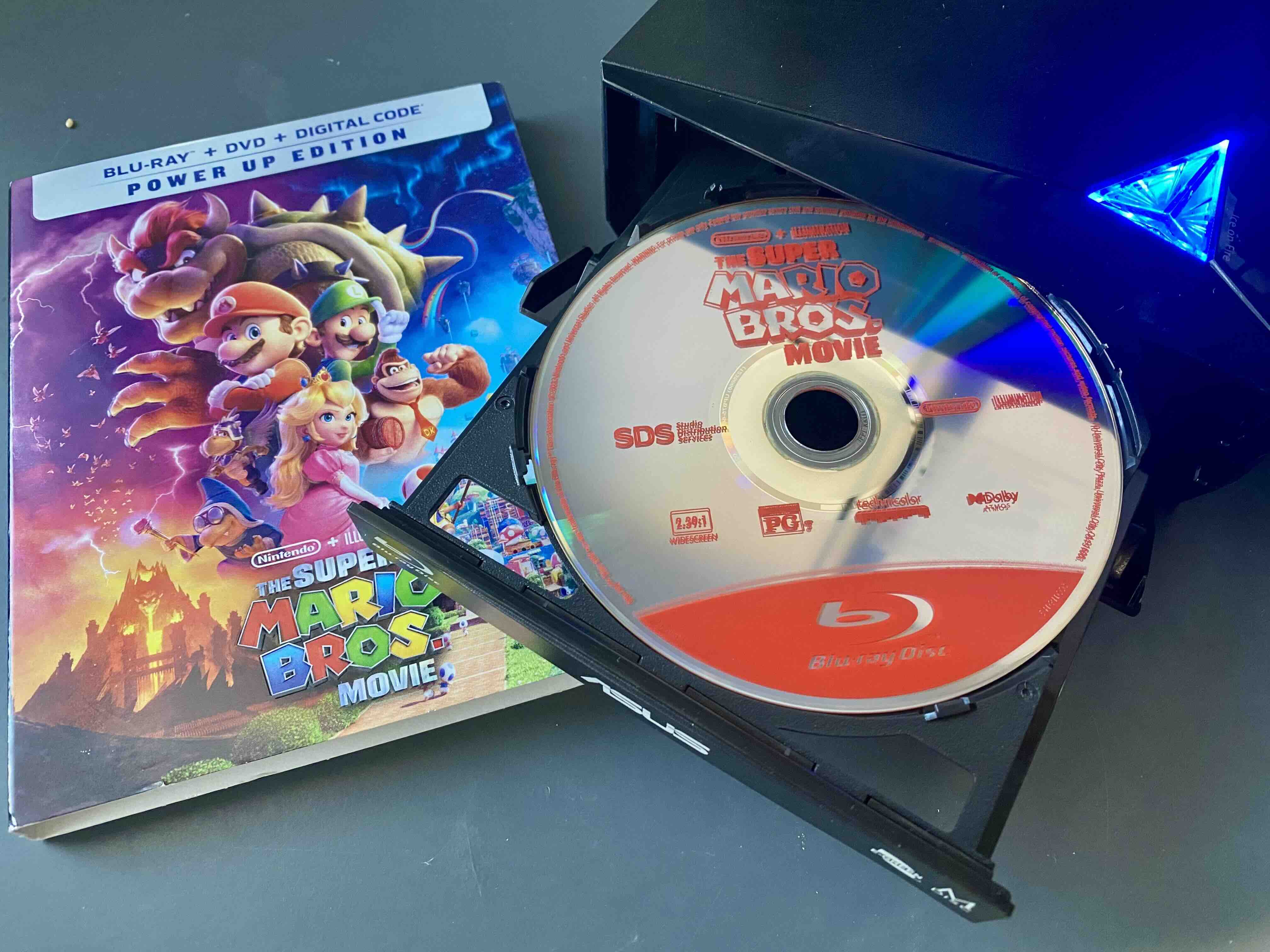A photo of the Blu-ray disc for the Super Mario Bros. Movie in an external Blu-ray drive next to the box art.