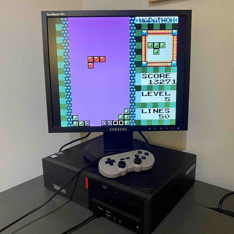 A photo of a Lenovo ThinkCentre PC tower sitting on a desk with an LCD monitor on top of it with a Super Nintendo controller.